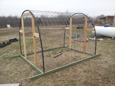 an outdoor chicken coop in the middle of a field with wire and wood posts around it