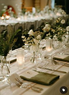 the table is set with silverware and white flowers in vases, napkins and candles