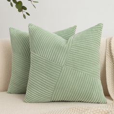 two green pillows sitting on top of a white couch next to a plant in a vase