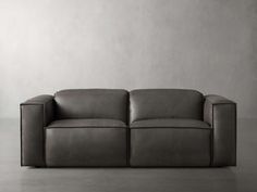 a black leather couch sitting on top of a floor next to a white wall in an empty room