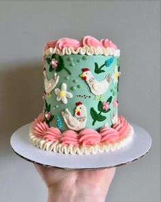 a hand holding a cake decorated with hens and flowers