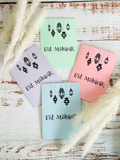 three different colored cards with arabic writing on them next to some pamy white feathers