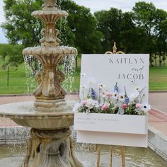 a fountain with flowers and a sign on it