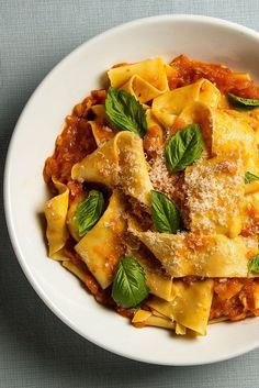 a white bowl filled with pasta covered in sauce and basil garnished with parmesan cheese