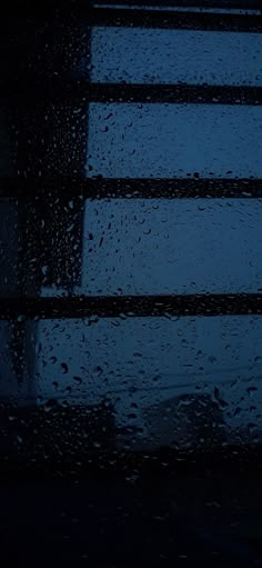 rain drops on the window as it is dark and drizzled with blue light