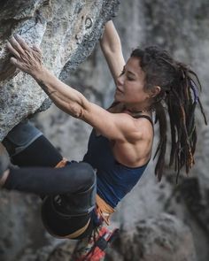 a woman climbing up the side of a rock with dreadlocks on her hands