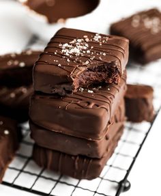 chocolate desserts stacked on top of each other on a cooling rack with white frosting