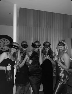 black and white photograph of four women in costumes posing for a photo with a clock behind them