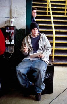 a man sitting on top of a black box next to a stair case and phone