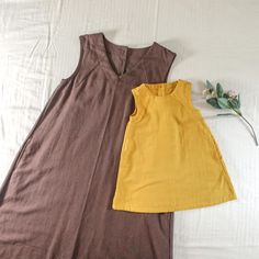 two women's dresses laying on top of a bed next to each other, one yellow and the other brown