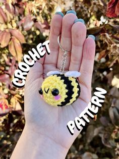 a hand holding a small crochet keychain with a bee on it