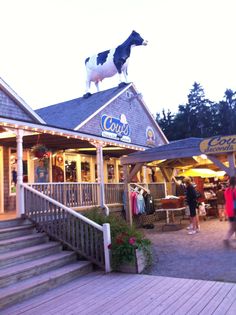 a cow statue on top of a building with people walking around the front porch and stairs leading up to it