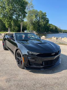 a black chevrolet camaro convertible parked in front of a lake