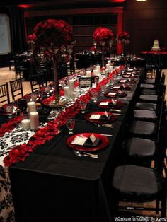 a long table is set with black chairs and red roses on the tablecloths