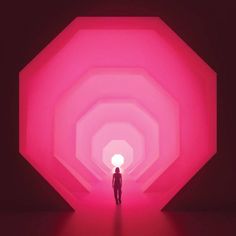 a person standing in the middle of a tunnel with bright pink light at the end