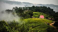 a house on top of a green hill surrounded by fog and low lying clouds in the distance