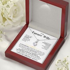 an open box with a necklace in it on a table next to flowers and a white rose