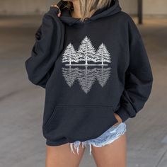 Wrap yourself in the cozy embrace of nature with our Pine Tree Hooded Sweatshirt! This sweatshirt features a stunning graphic of three majestic pine trees, with their reflection dancing off the tranquil waters of a serene lake. It's the perfect gift for nature lovers, adventurers, and hiking enthusiasts alike. Whether you're strolling through the woods, embarking on a scenic hike, or simply cozying up by the campfire, this sweatshirt is your go-to companion for all outdoor adventures. Embrace th Graphic Print Tops For Outdoor Winter Activities, Graphic Print Tops For Outdoor Winter, Casual Outdoor Tops With Kangaroo Pocket, Oversized Tops With Drawstring Hood For Outdoor, Winter Hoodie For Outdoor Activities, Fall Outdoor Hoodie Tops, Fall Hoodie Top For Outdoor, Hoodie Top For Outdoor Fall Activities, Hoodie Top For Outdoor Fall Events