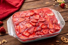 a glass dish filled with sliced strawberries on top of a wooden table next to pretzels