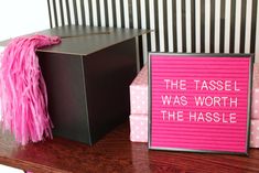 a pink sign sitting on top of a wooden table next to a black and white box