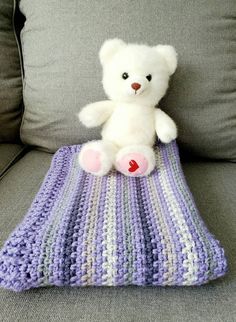 a white teddy bear sitting on top of a crocheted blanket