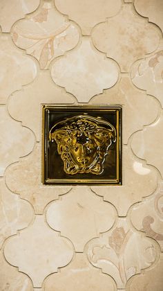 a tile wall with a gold lion head in the center and an intricate design on it