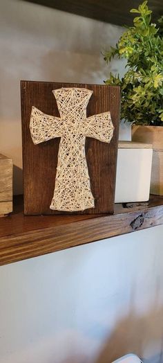 a wooden cross sitting on top of a shelf next to a potted plant in a vase