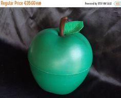 an apple shaped container with a green leaf on the top, sitting on a black surface