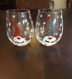 two wine glasses decorated with gnomes and snowflakes on a wooden table top