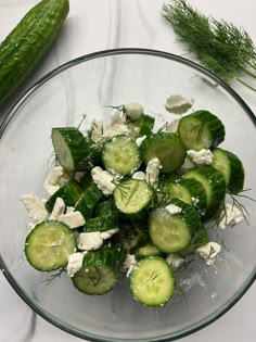 cucumbers, cheese and dill in a glass bowl on a white table