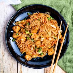 a black plate topped with noodles and meat next to chopsticks on a wooden table