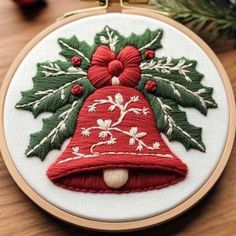 a christmas bell ornament with holly leaves and bells on it is hanging from a wooden hoop