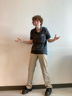 a young man standing in front of a white wall with his hands out to the side