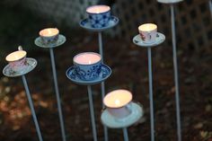 tea cups and saucers are arranged on sticks with lit candles in the middle, surrounded by other teacups