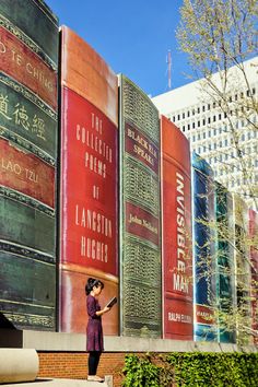 a woman is standing in front of several books on the side of a large building