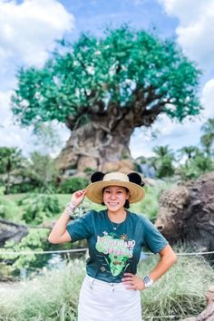 a woman wearing a hat standing in front of a tree