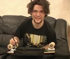 a young man sitting on a couch holding two skateboards and smiling at the camera