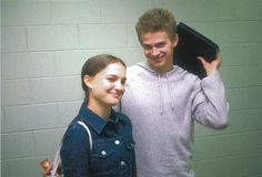 a man and woman standing next to each other in front of a white brick wall