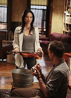 a woman is playing the violin while another man sits on the floor in front of her