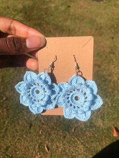 a pair of blue crocheted flower earrings being held by someone's hand