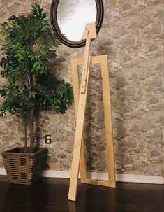 a wooden easel stands next to a potted plant in front of a stone wall