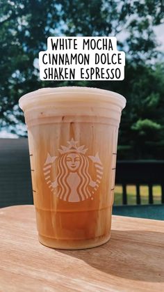 a cup of iced coffee sitting on top of a wooden table next to a tree