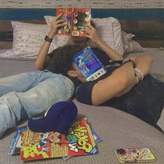 a man laying on top of a bed reading a book next to another person lying down