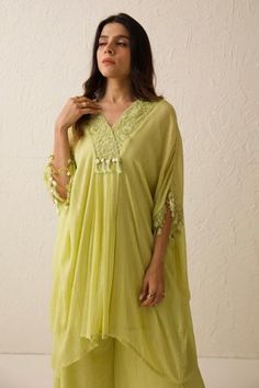 Lime green chanderi kaftan with front plated details, tonal floral pattern dabka, dori, sequin embroidered V neck and sleeve borders. Paired with flared pants and inner slip.
Components: 3
Pattern: Embroidered
Type Of Work: Dori, Dabka and Sequin Work
Neckline: V Neck
Sleeve Type: Kaftan: Batwing Sleeves, Inner Slip: Sleeveless
Fabric: Georgette Tissue
Color: Green
Other Details: 
Fringe tassel details
Occasion: Puja,Work - Aza Fashions Peach Kurti, Women Nightwear Dresses, V Neck Kaftan, Festival Dresses, Kaftan Pattern, Kaftan Designs, Latest Dress Design, Trendy Shirt Designs, Casual Indian Fashion