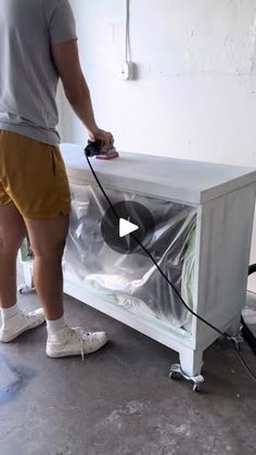 a man in yellow shorts is using a vacuum to clean a white table with a black cord