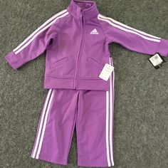 Purple Toddler Adidas Tracksuit Set. The Set Features A Full Zip Front Raglan Jacket With Dazzle Applied Stripes, Princess Seams, And Scoop Pockets. Embroidered Adidas Brand Mark On Left Chest And On The Back Of The Jacket. Elastic Waist Pant With Dazzle Applied Stripes And Embroidered Adidas Brand Mark On Left Leg. Nwt 12 Months Adidas Fitted Long Sleeve Sets, Adidas Fitted Playwear Sets, Adidas Fitted Sets For Playwear, Adidas Fitted Winter Sets, Winter Adidas Fitted Sets, Raglan Jacket, Toddler Adidas, Brand Mark, Adidas Tracksuit