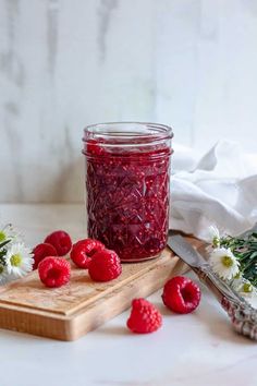 raspberry jam in a jar with fresh flowers on the table next to it