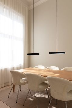 a dining room table with white chairs and hanging lights