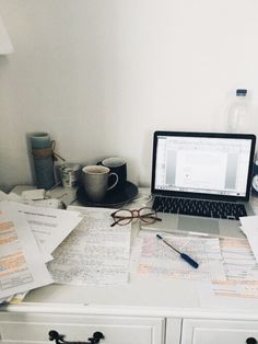 an open laptop computer sitting on top of a white desk covered in papers and paperwork