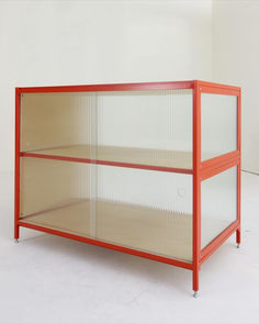 a red metal shelf with two shelves on each side, against a white wall in an empty room